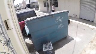 A naked chick is having fun behind the garbage tank