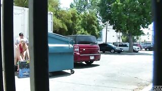 A naked chick is having fun behind the garbage tank