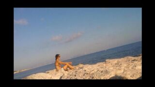A completely naked girl sunbathes on the beach and caresses her body
