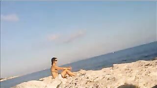 A completely naked girl sunbathes on the beach and caresses her body