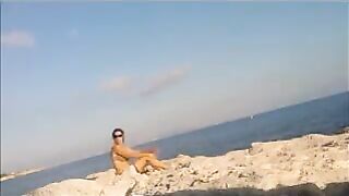 A completely naked girl sunbathes on the beach and caresses her body