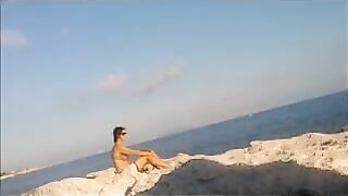 A completely naked girl sunbathes on the beach and caresses her body