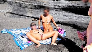 A girl removes her swimsuit and rubs herself while her friend jerks off on the beach